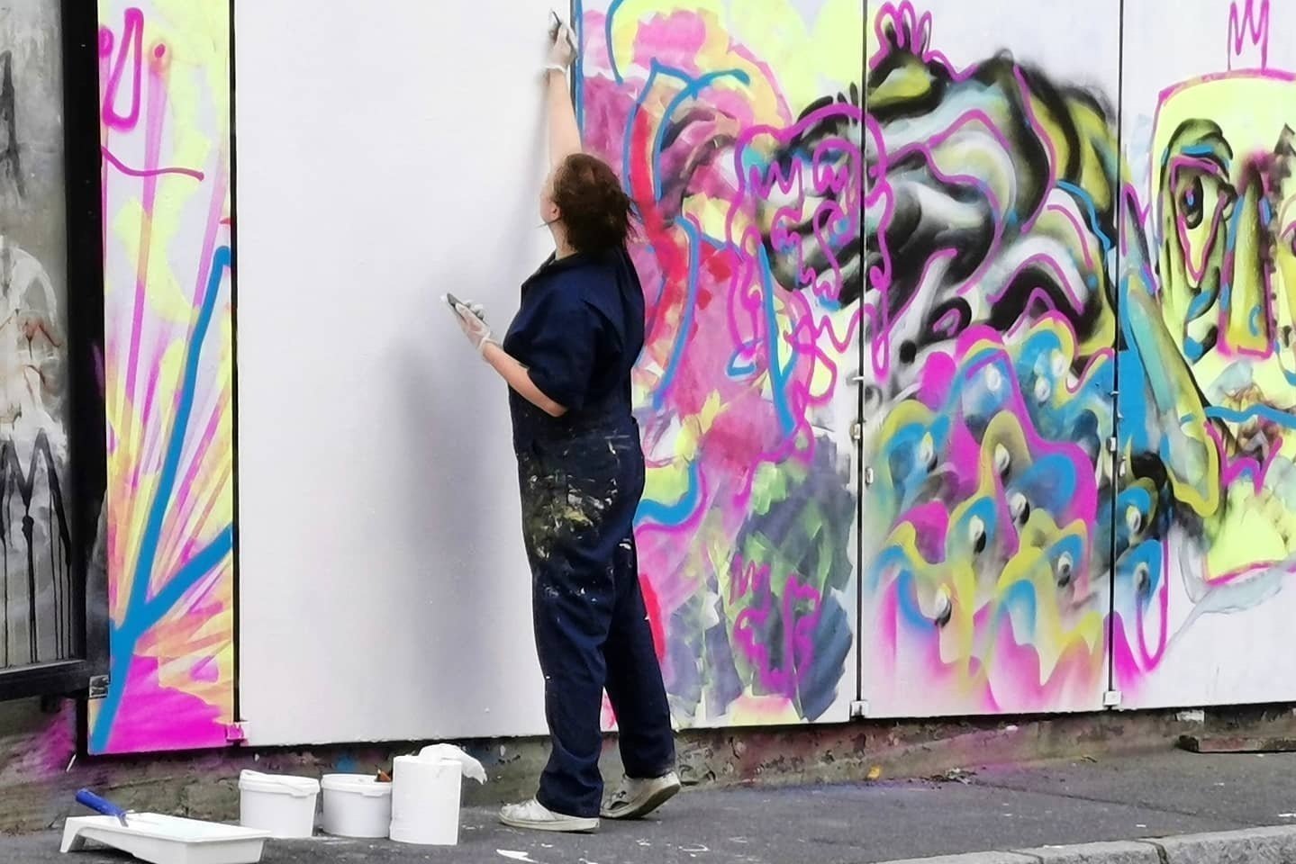 En kunstner maler en fargerik vegg med graffiti på en utendørs mur.