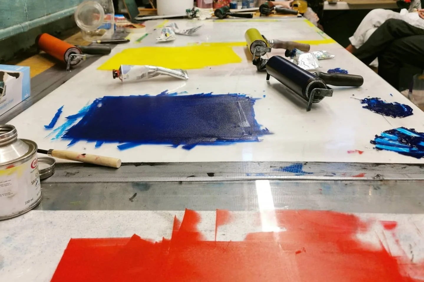 Arbeidsbord med lerret og spraymale i ulike farger, maling spruter og verktøy brukt til maling.