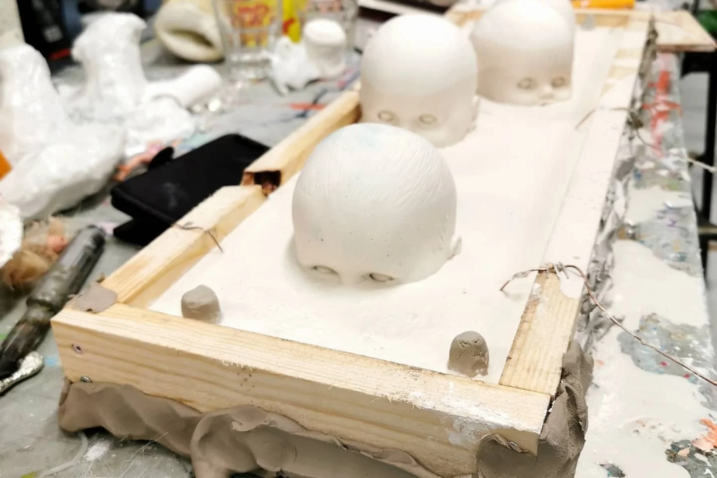 Keramikkunstverk i produksjon med flere hvite keramikkhoder på en arbeidsflate med verktøy og materialer rundt.