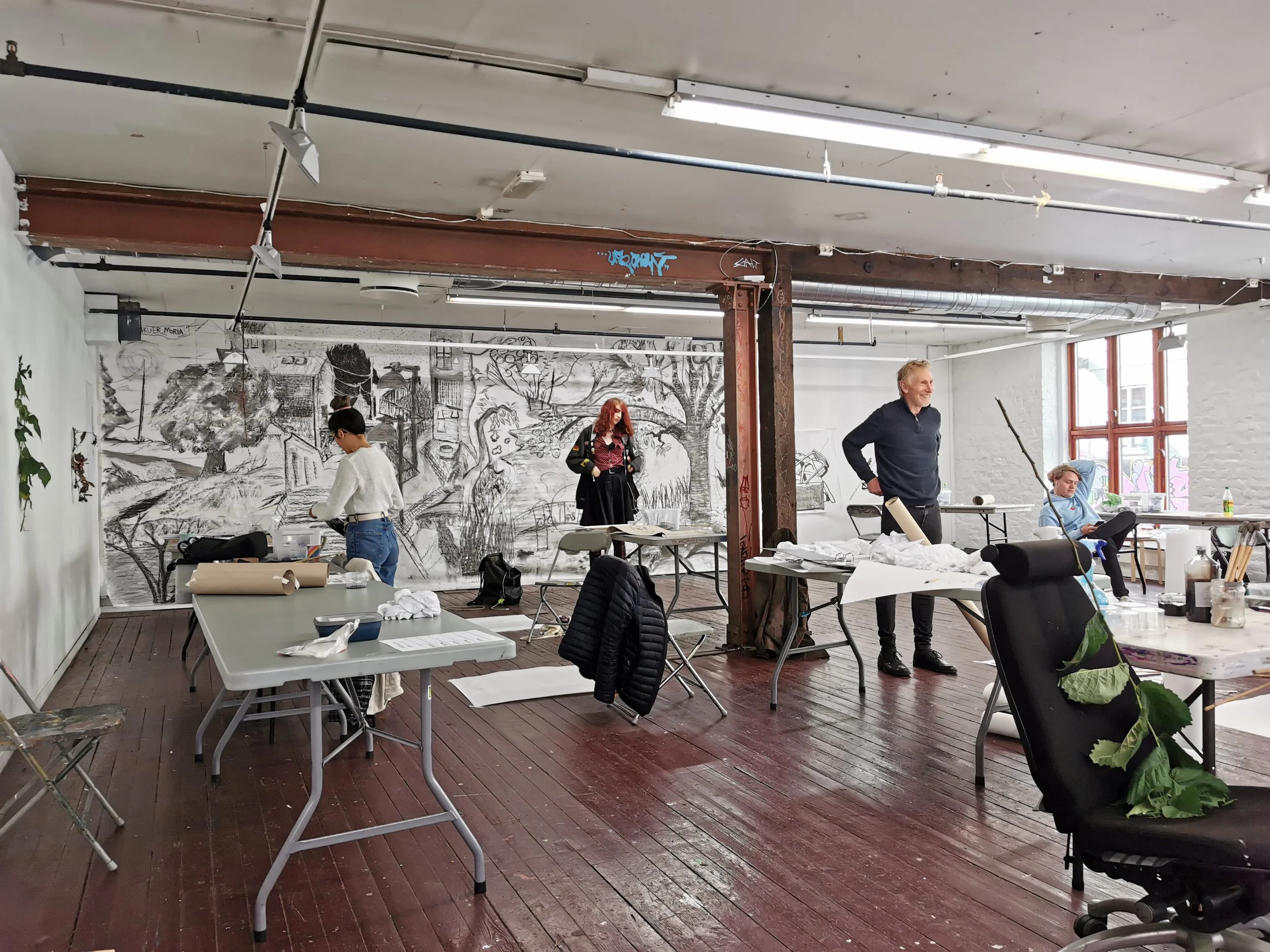 En gruppe mennesker i et rom med møbler og kunst på veggen, som forbereder seg til en utendørsaktivitet eller kunstprosjekt.