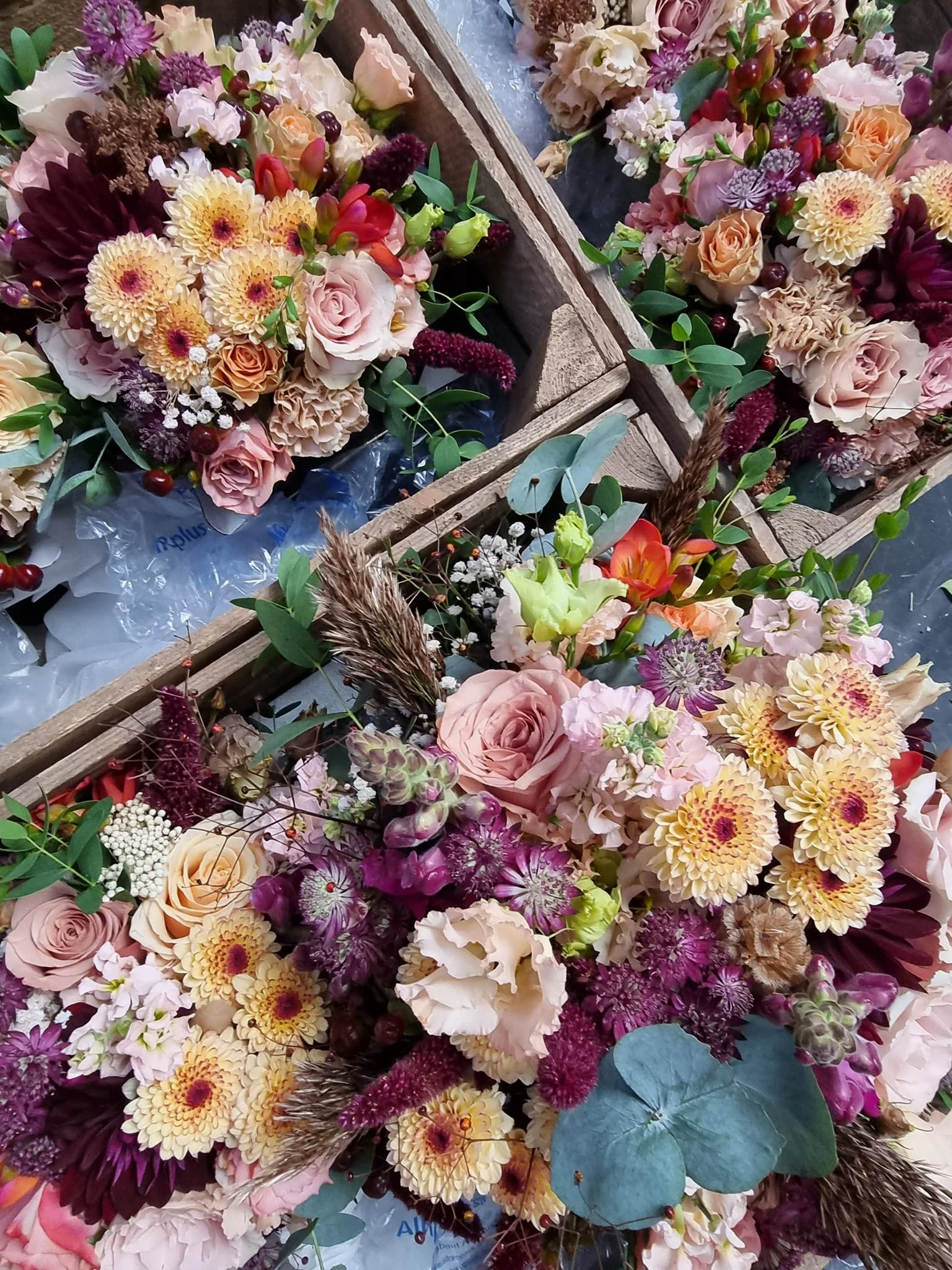 Multiple vibrant flower arrangements in wooden crates, featuring roses, chrysanthemums, lisianthus, astilbe, eucalyptus, and other mixed flowers.