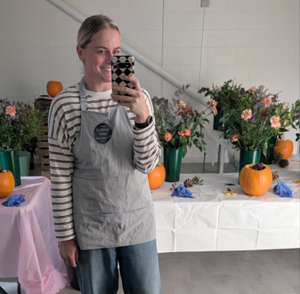 A woman taking a selfie in front of a table decorated with flowers and pumpkins.