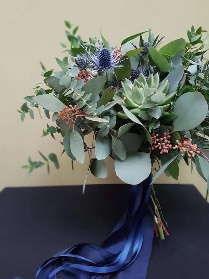 A bouquet of assorted flowers and greenery tied with a blue ribbon on a dark surface.