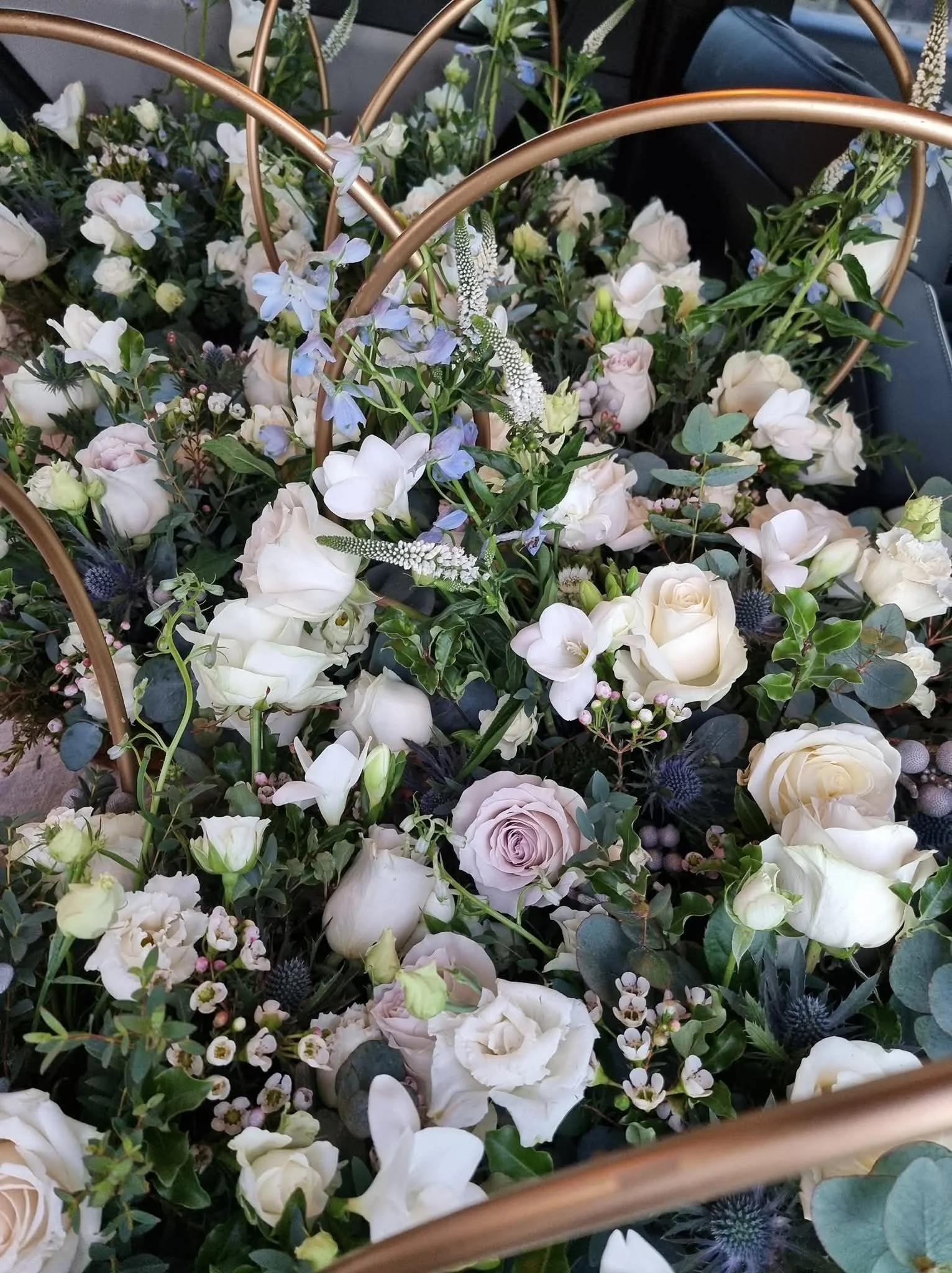 A bouquet of white and pastel-colored roses, lilies, and other flowers with greenery and gold-colored handles.