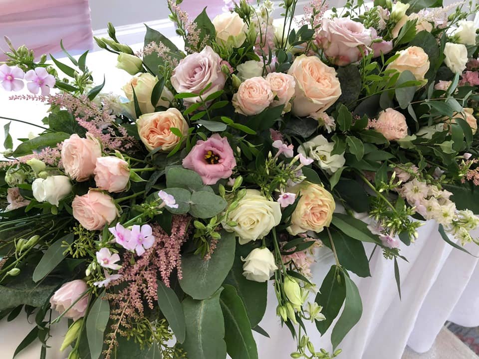 A large floral arrangement with pink, peach, and white roses, lisianthus, and greenery on a white surface.