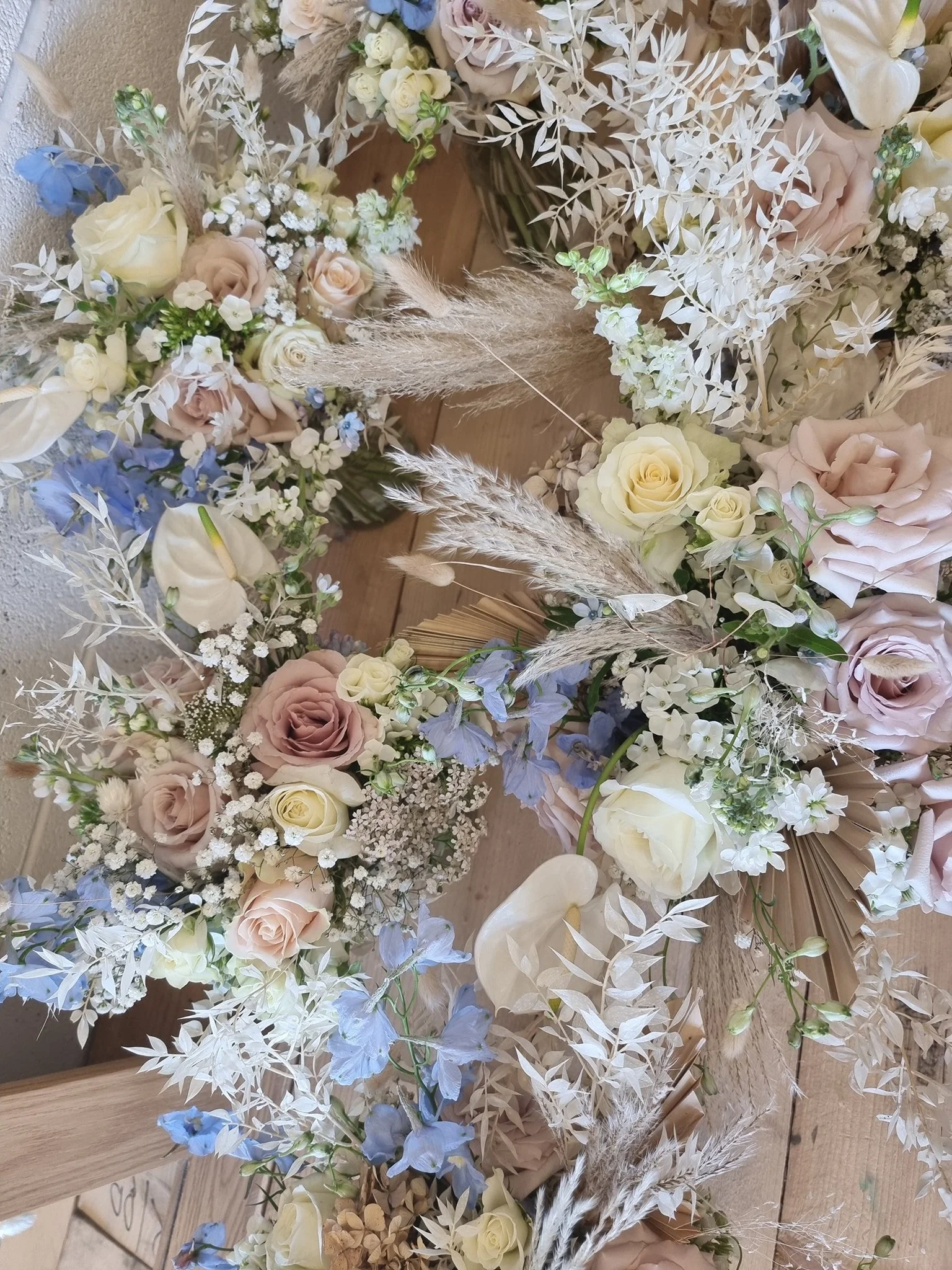 A floral arrangement with roses, baby's breath, dried grasses, and other seasonal flowers in soft pastel colors, on a wooden surface.