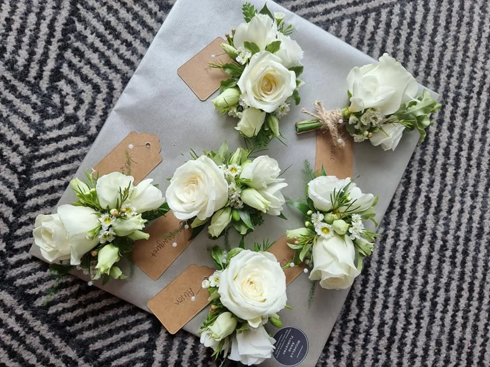 Multiple white flower corsages arranged on a wrapped gift box, placed on a black and white striped fabric surface.