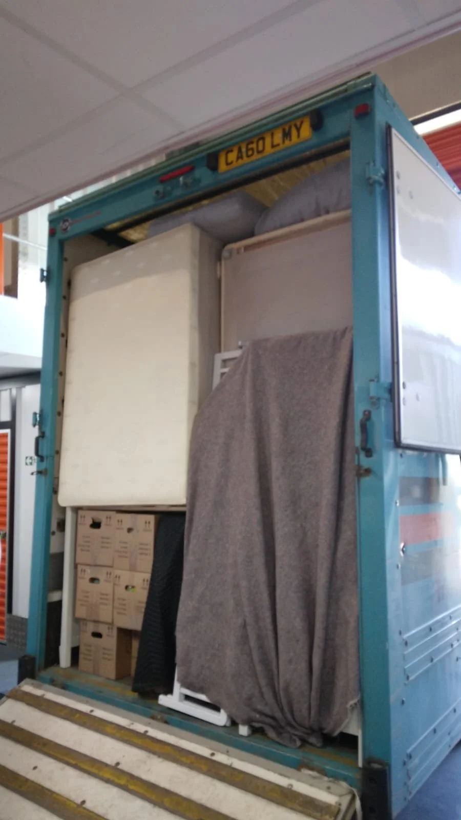 Open moving truck loaded with boxes, furniture, and a covered item in a gray blanket, parked indoors.