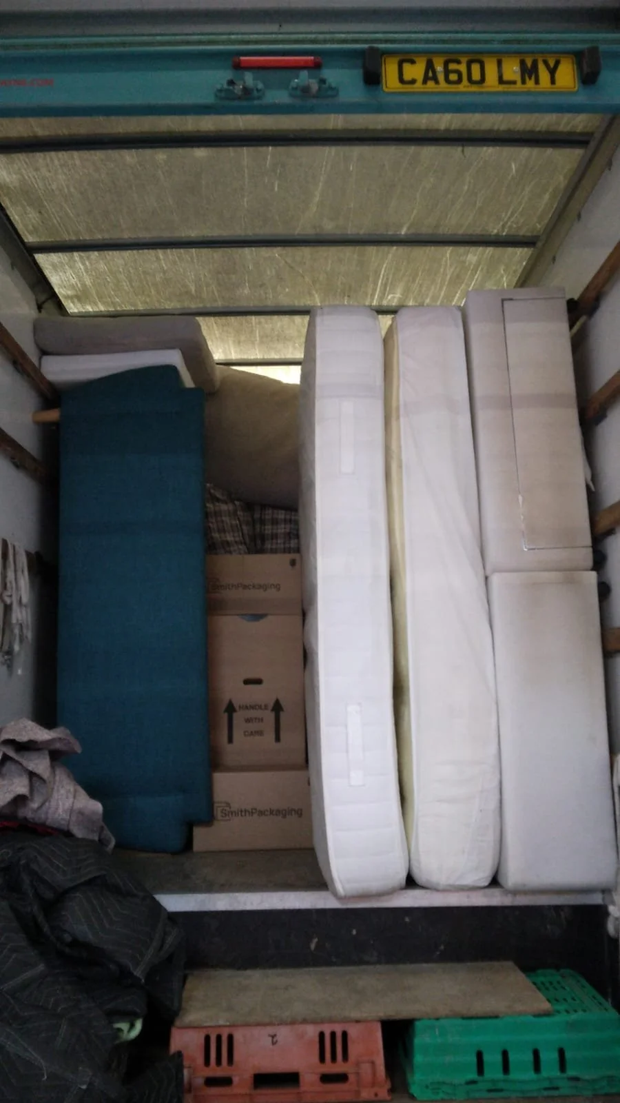 U-Haul truck interior loaded with mattresses, cardboard boxes, clothes, and plastic crates.