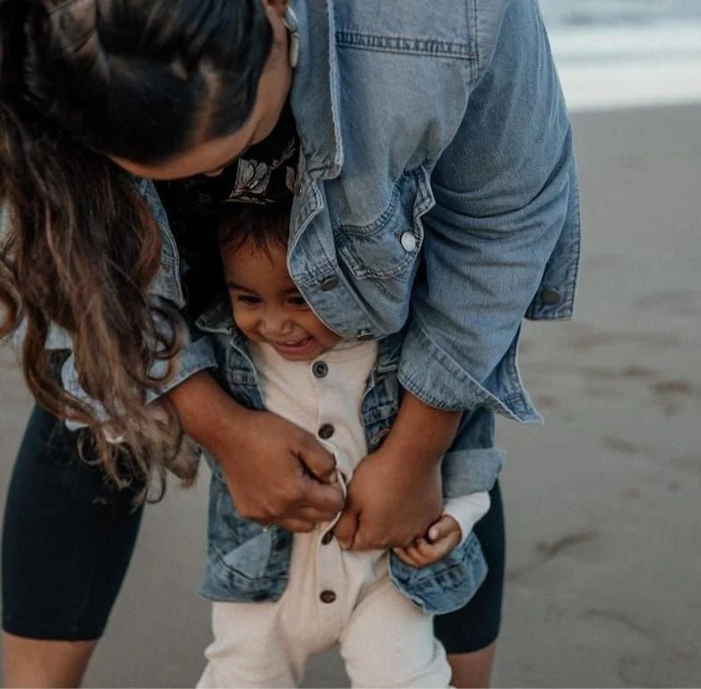 Child laughing while being playfully held and pulled by an adult on a beach.