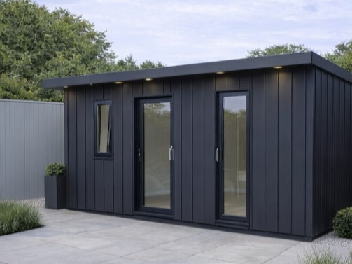 A completed Steel Frame Garden Room with a flat roof and large windows, situated on a concrete patio with greenery around.