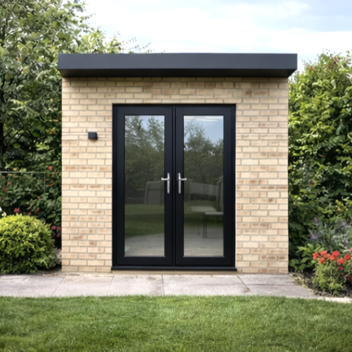 Garden Room Frame finished with brick and with double glass doors, black trim, and a black roof, set in a garden with bushes and flowers.