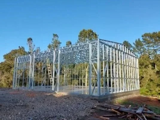 Steel framing construction site for a building, with trees and blue sky in the background.