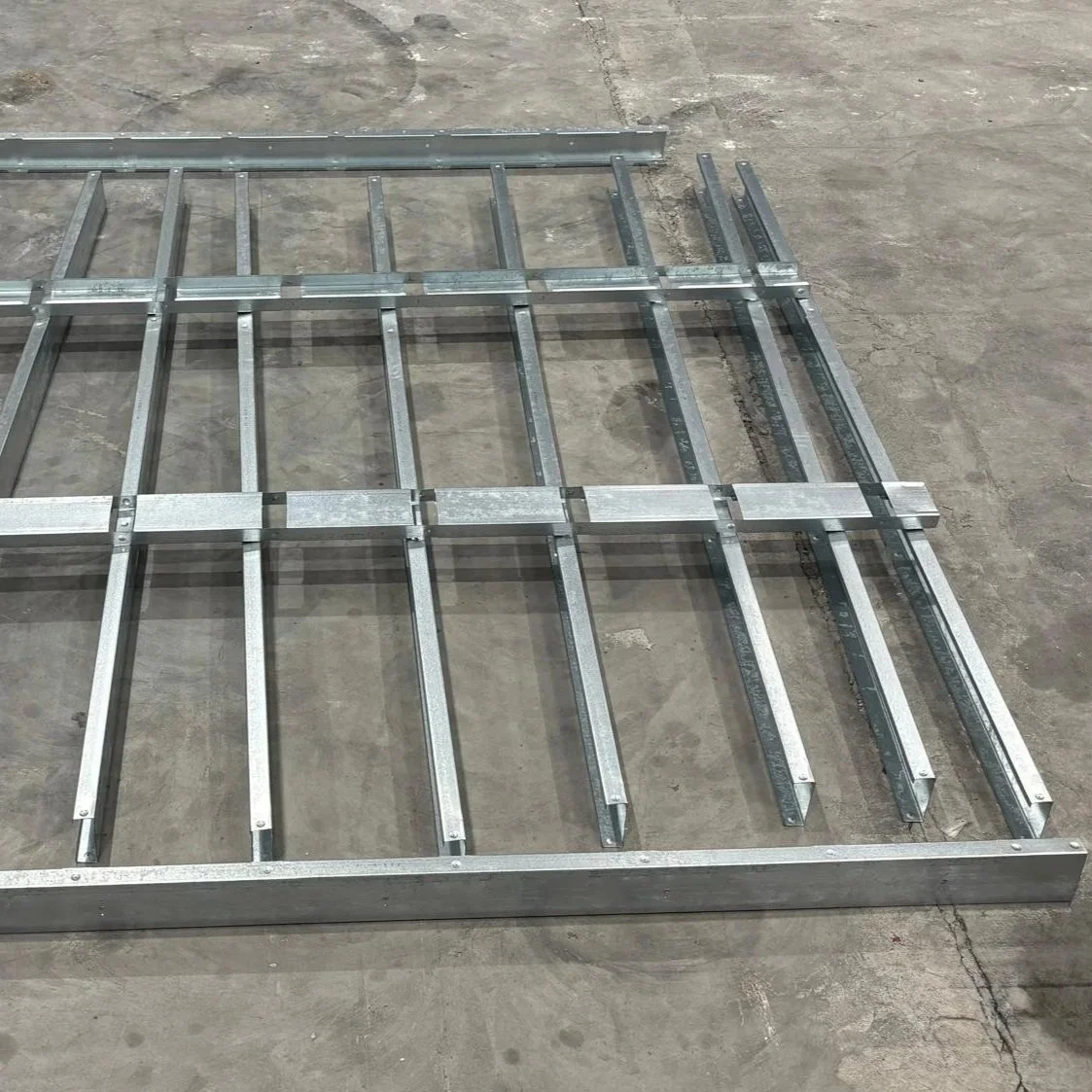 Metal framework parts laid out on a concrete floor, ready for assembly.