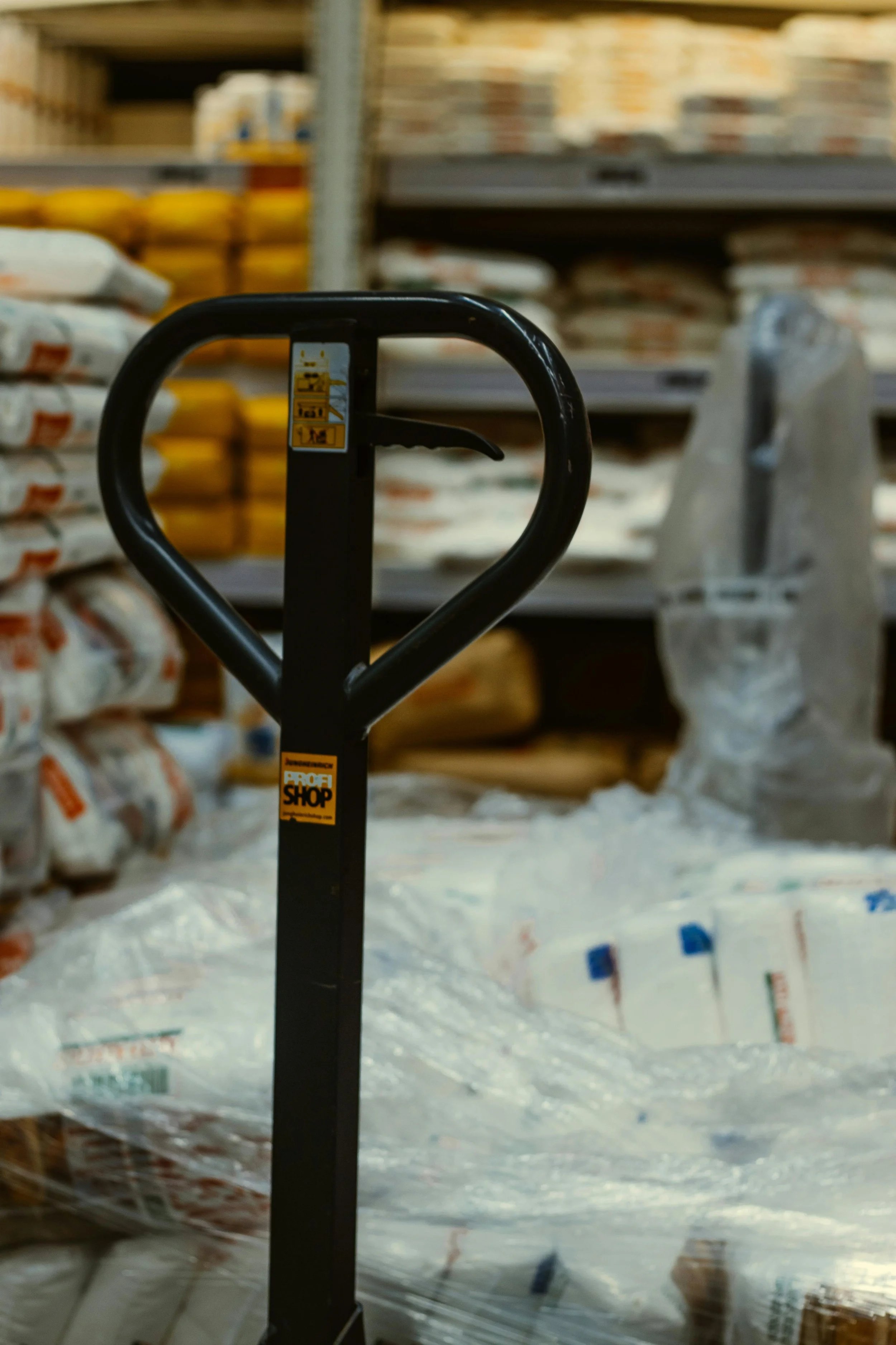 A black hand truck or dolly in a hardware store aisle, surrounded by bags of construction materials on shelves.