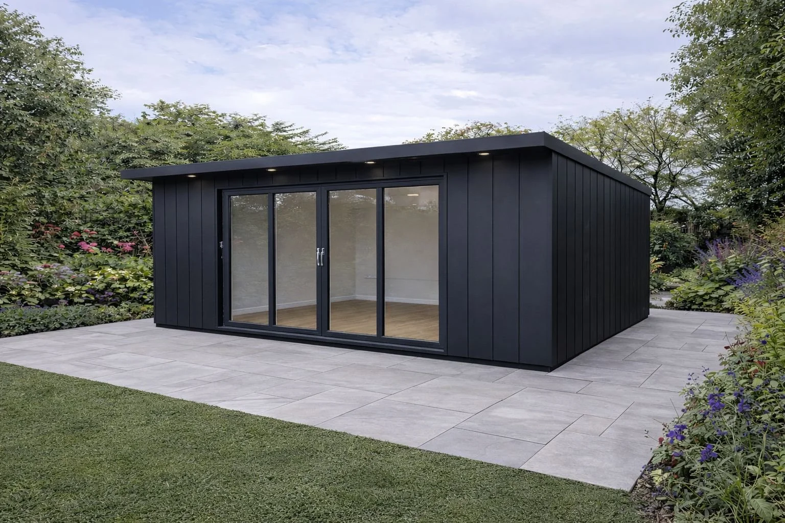 A completed Steel Frame Garden Room with large glass sliding doors, situated on a paved patio surrounded by greenery.