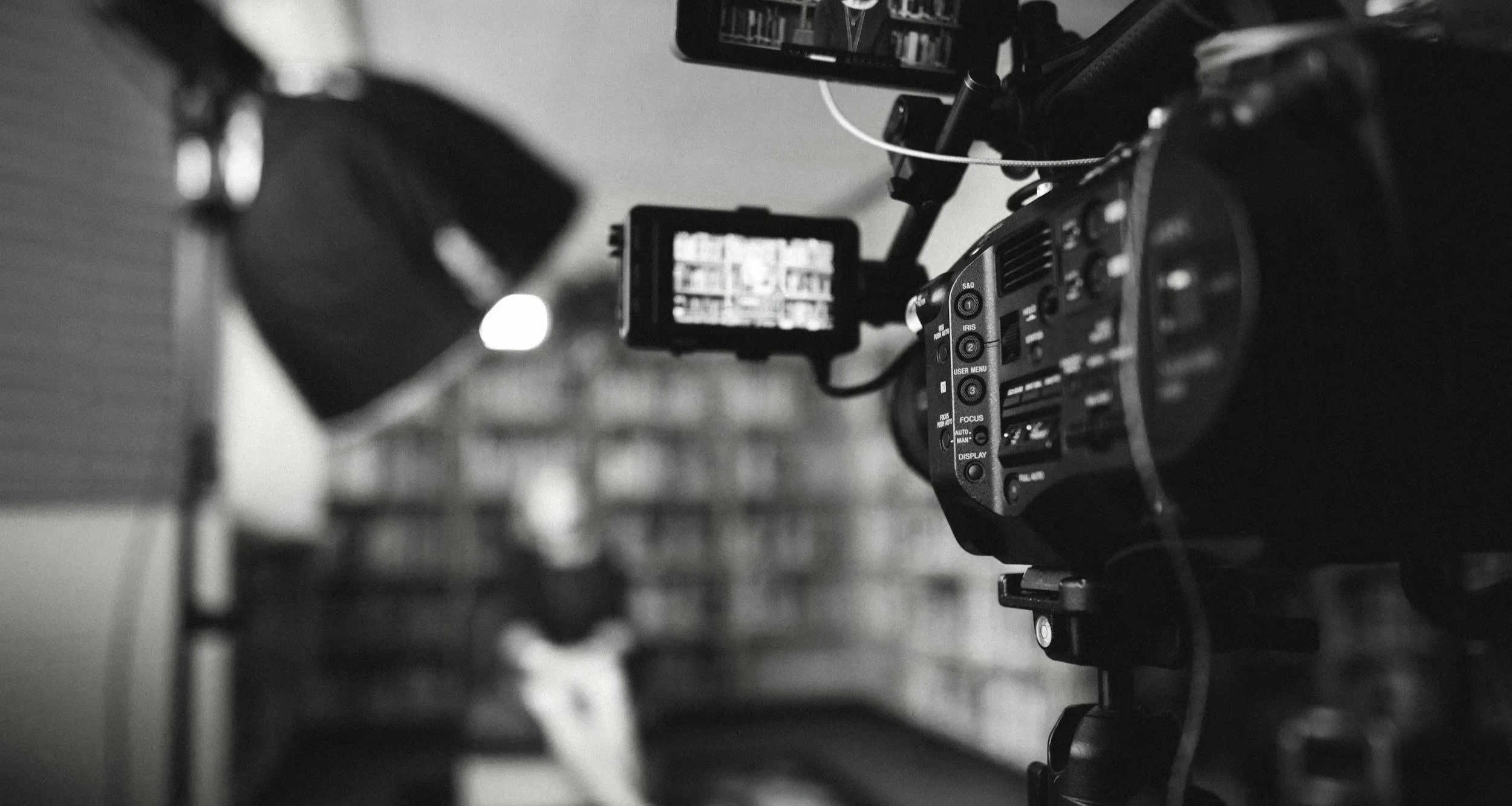 Black and white photo of a professional video camera setup in a library or bookstore with bookshelves in the background.