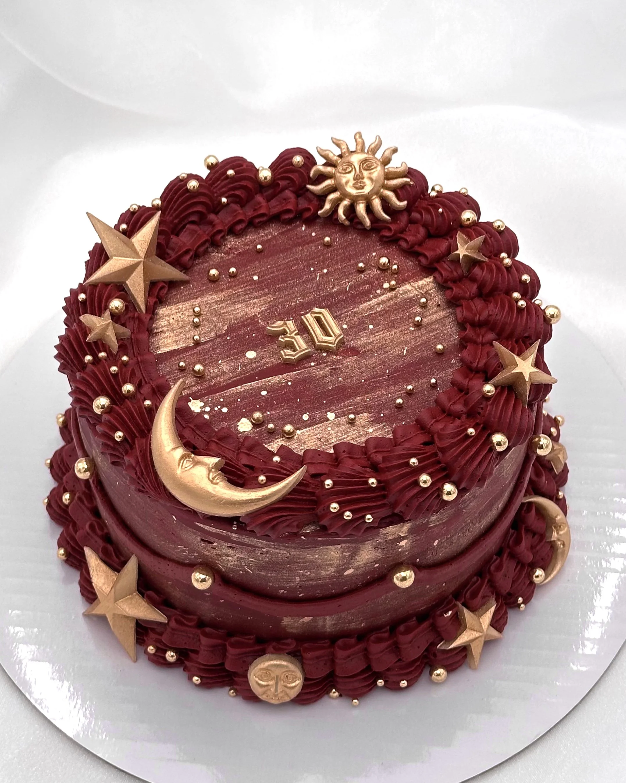 Burgundy cake with gold sun, moon, and star accents​​​​​​​​​​​​​​​​