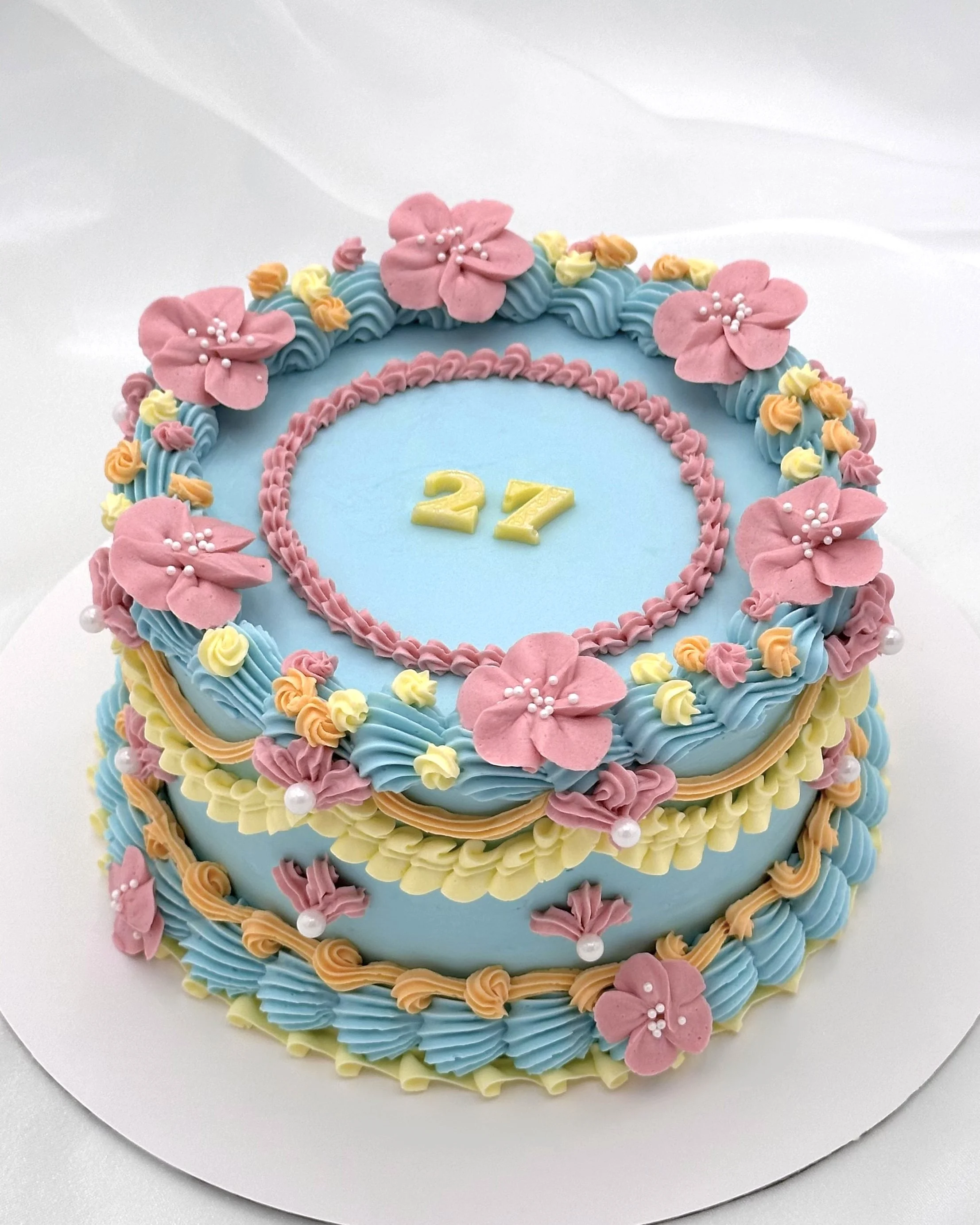 Blue cake with pink, orange, and yellow flowers and lambeth-style piping​​​​​​​​​​​​​​​​