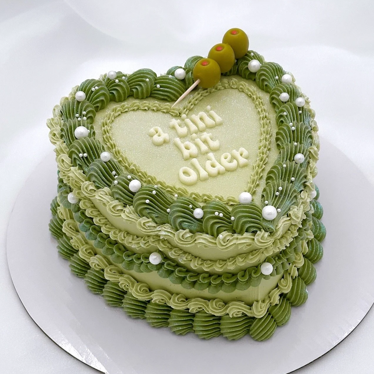 Green heart-shaped birthday cake with “a tini bit older” written on top.