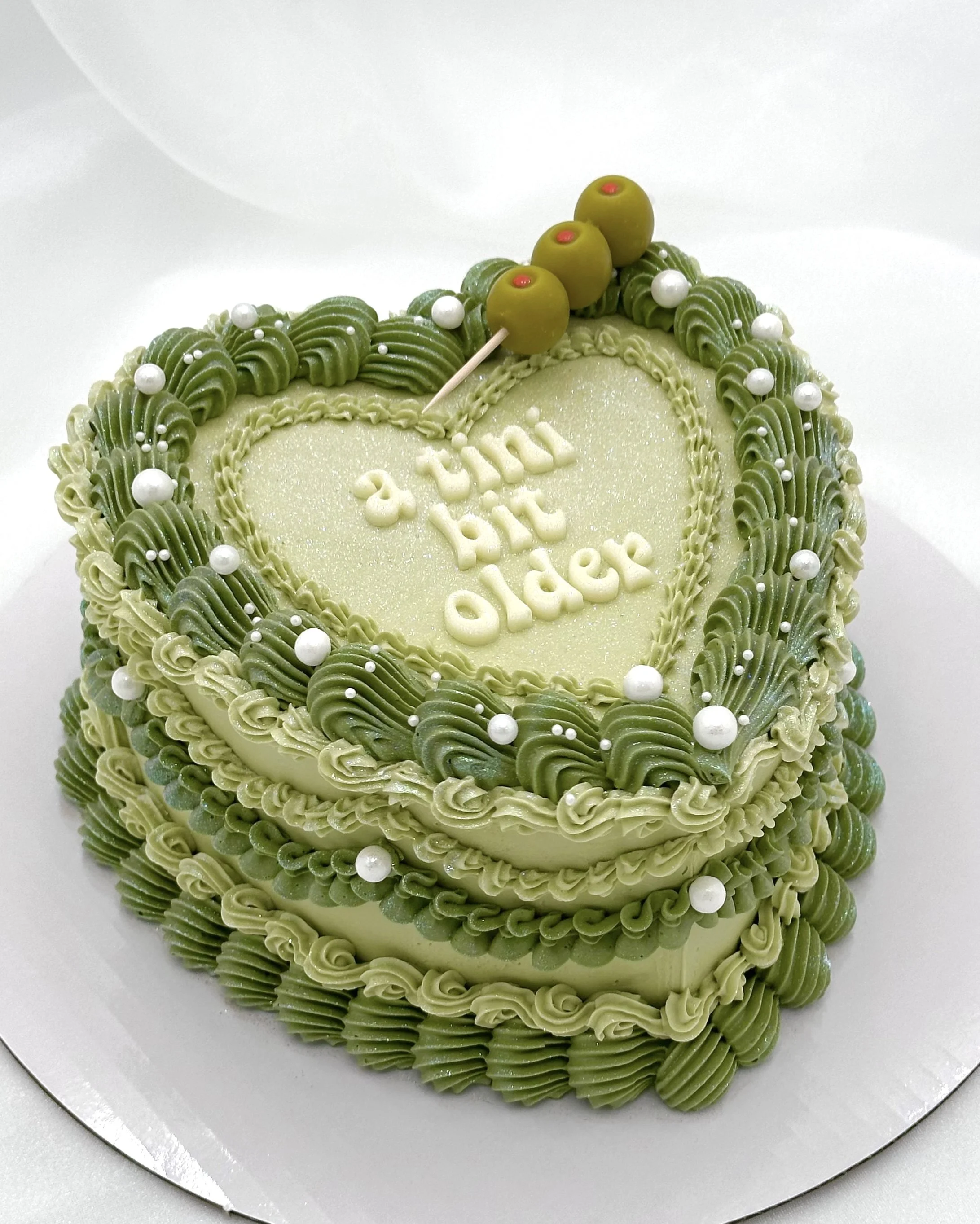 Green heart-shaped birthday cake with “a tini bit older” written on top.