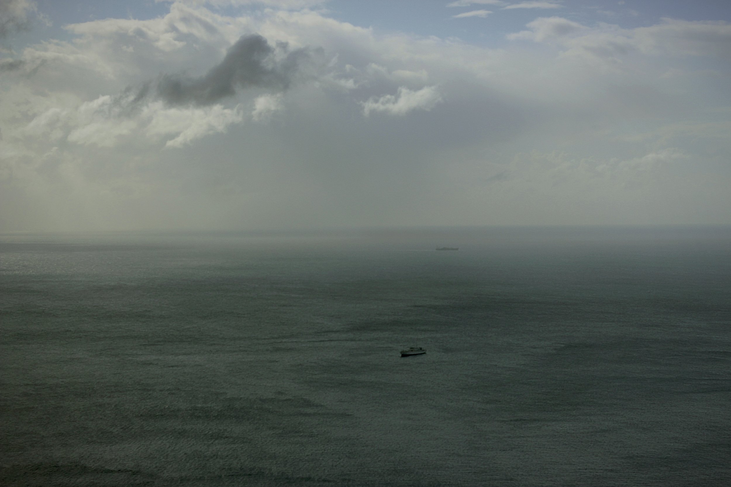 Overcast sky with dark clouds over the ocean, with a ship in the distance.