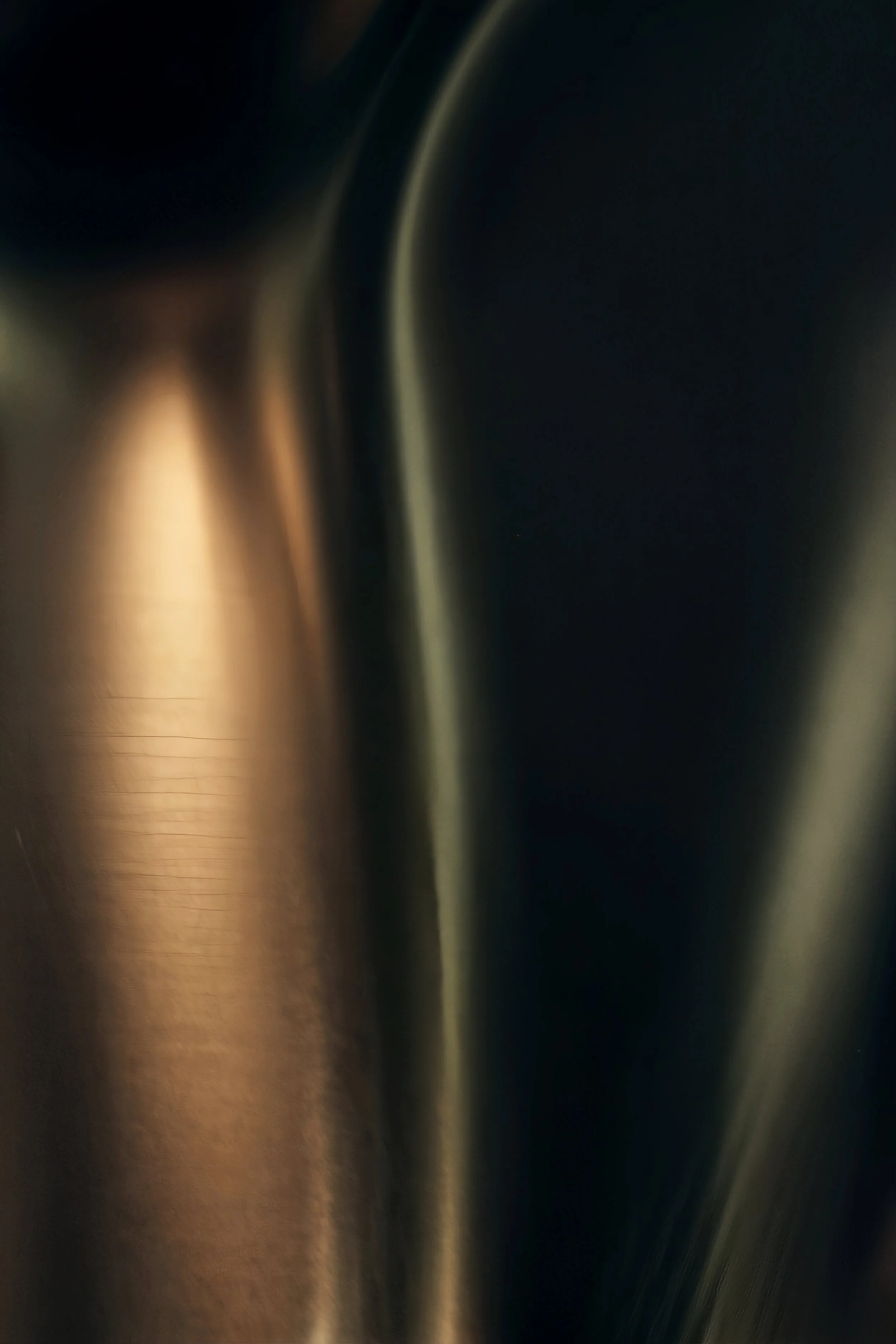 Close-up image of a metallic surface with curved lines, showing reflections and a gradient of dark and light areas.