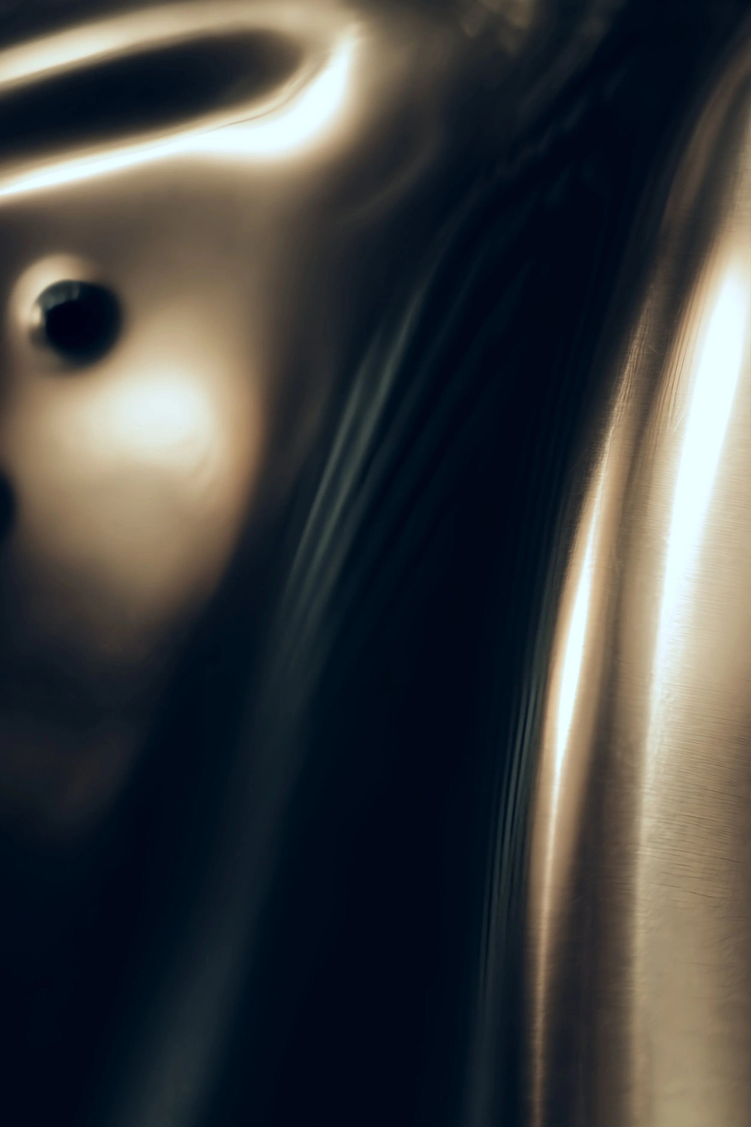 Close-up photo of a shiny, metallic surface with smooth curves and reflections.