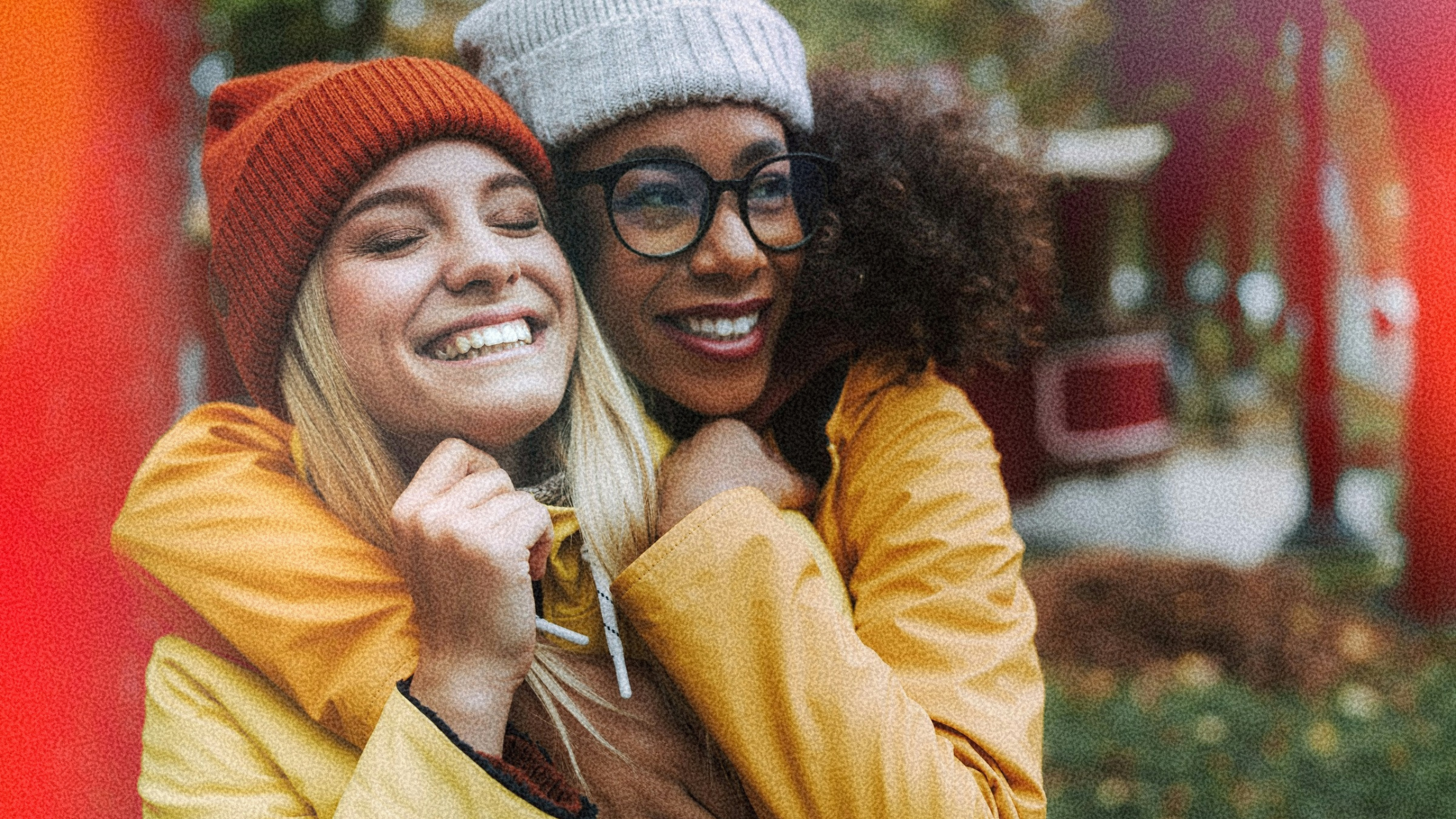 two women are smiling, wearing winter hats and hugging