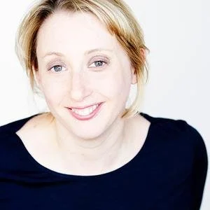 A smiling woman with blonde hair wearing a black top.