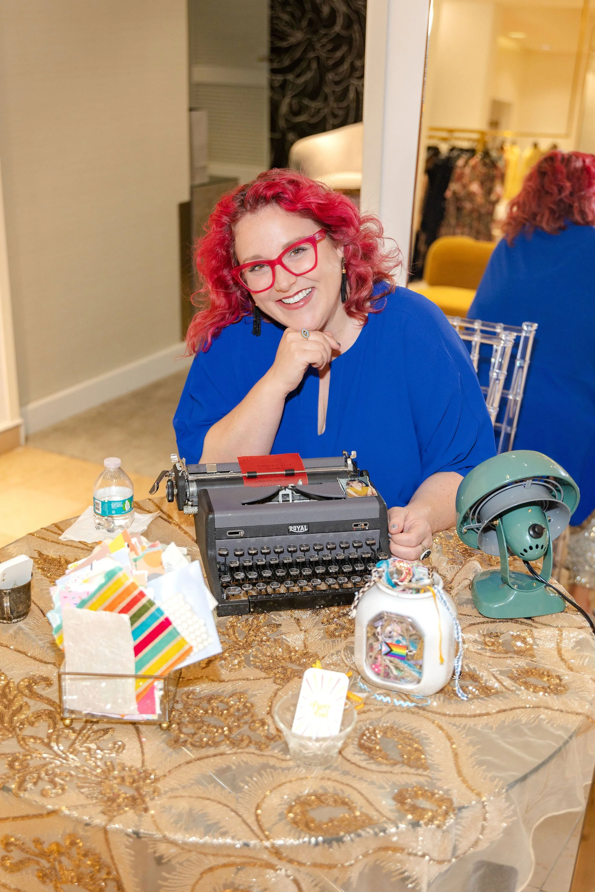 Smiling woman with red hair sitting at a table with a typewriter