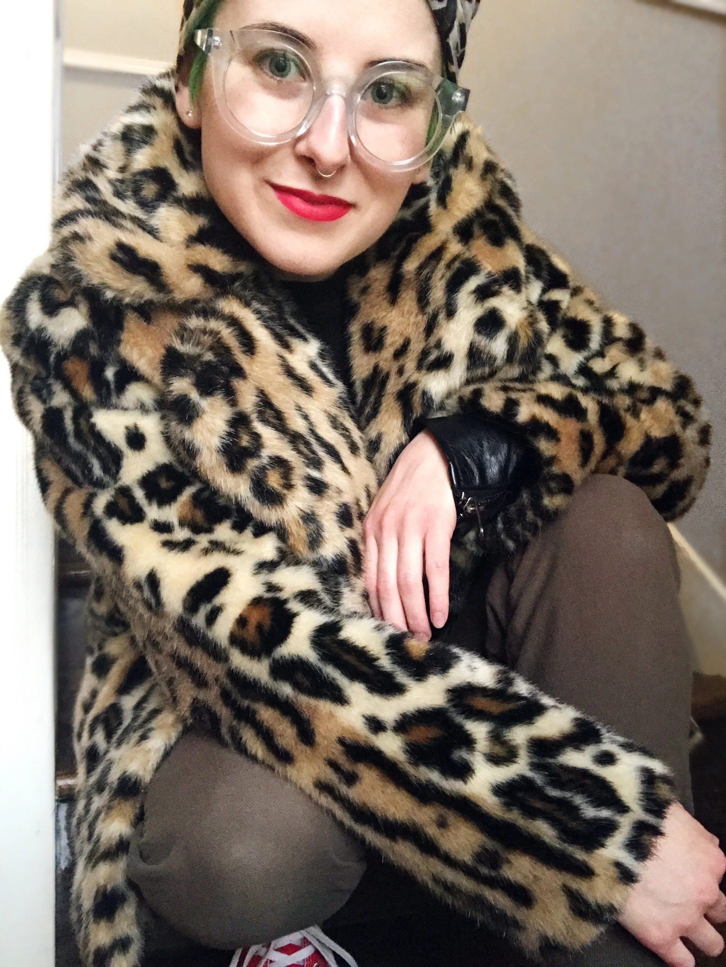 Photo of sydney in a leopard print coat and classes, crouched down and relaxed