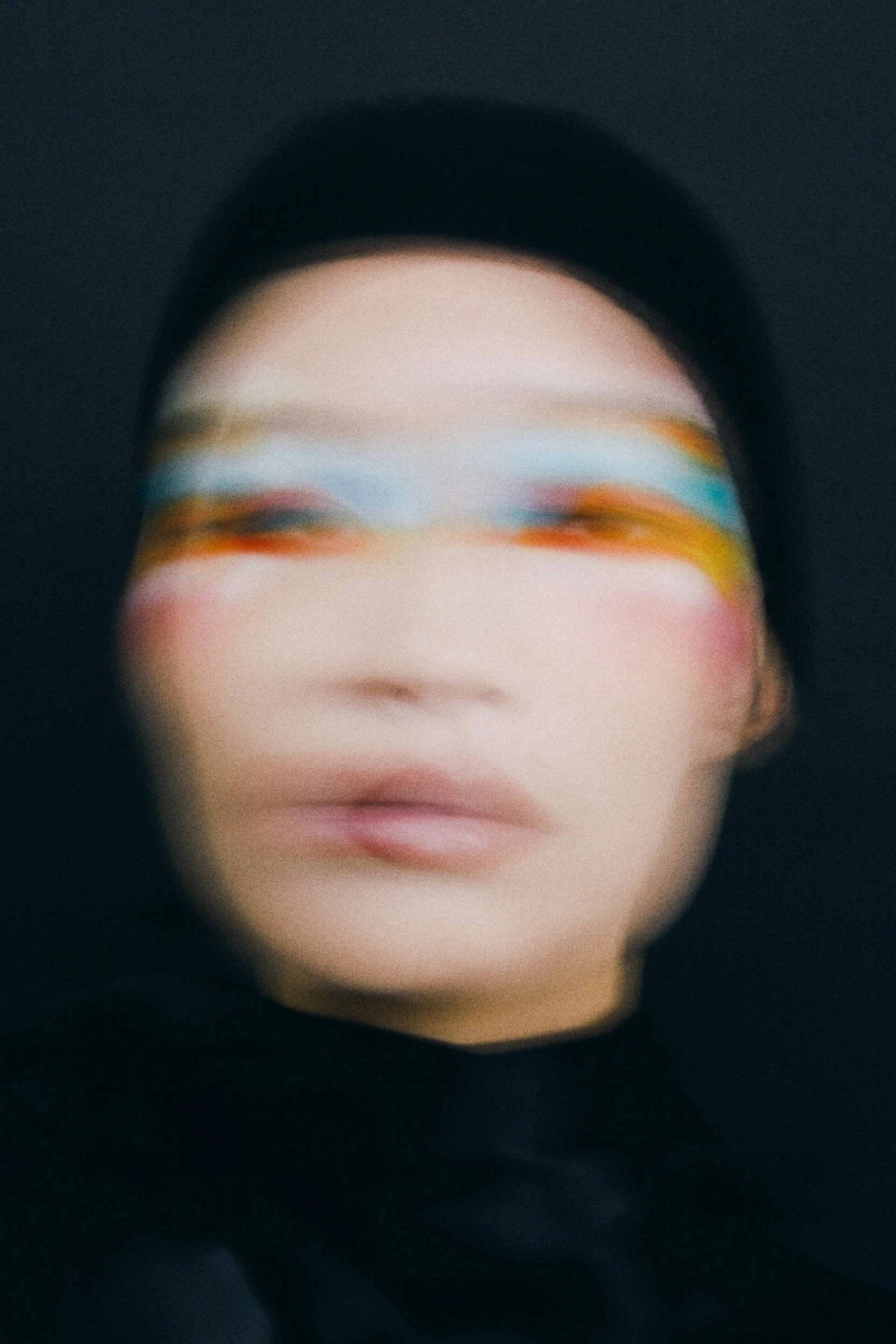A person wearing a black hat with painted sunglasses, blurry image, black background.