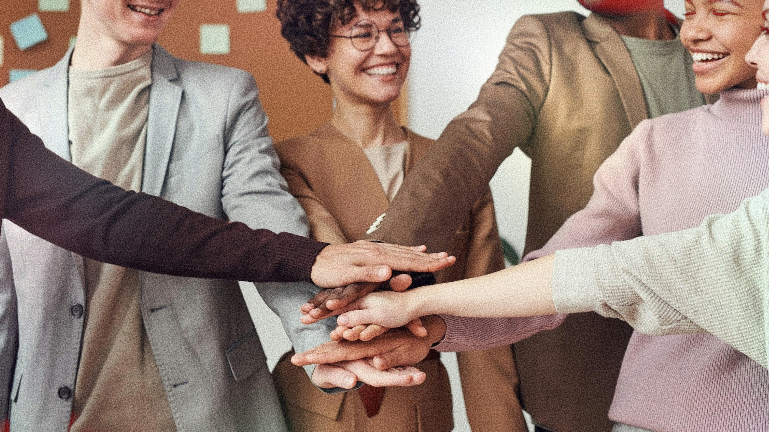 group of people all have their hands in like a team with a woman with short curly hair and glasses smiling in frame