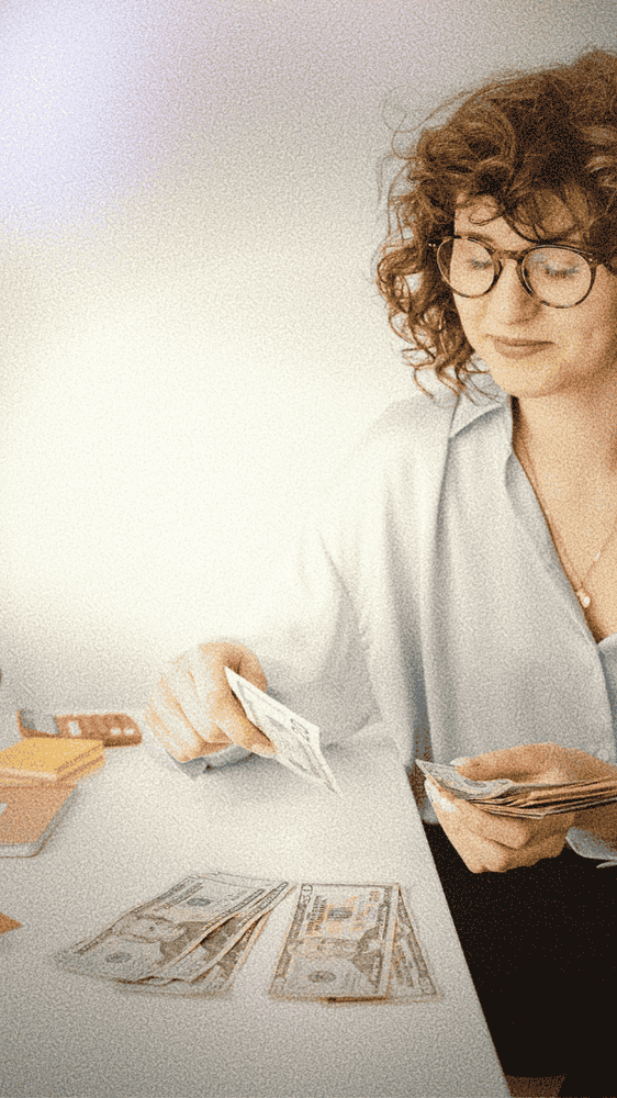 woman with curly brown hair and glasses smiling subtly while organizing her money