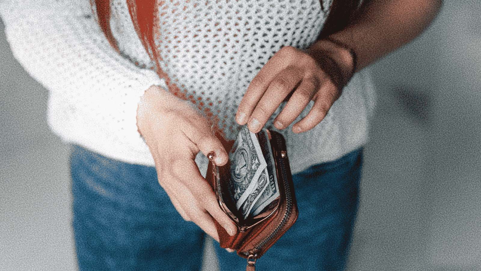 Person holding open wallet with dollar bills inside.