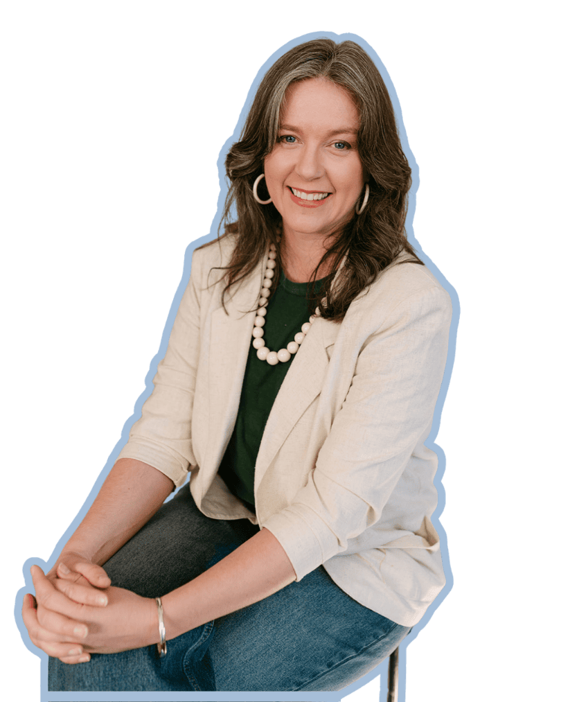 Woman with brown hair wearing a beige blazer, dark green top, white beaded necklace, and hoop earrings, smiling while sitting with her hands clasped.