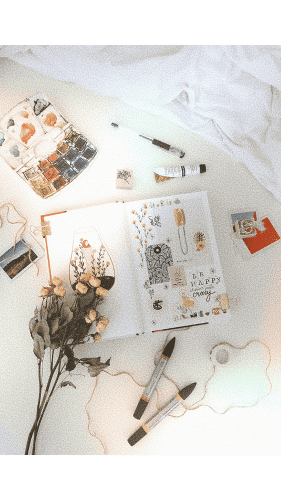 overhead image of an art journal with art supplies around it, a bouquet of small dried flowers, some twine, and a few photos