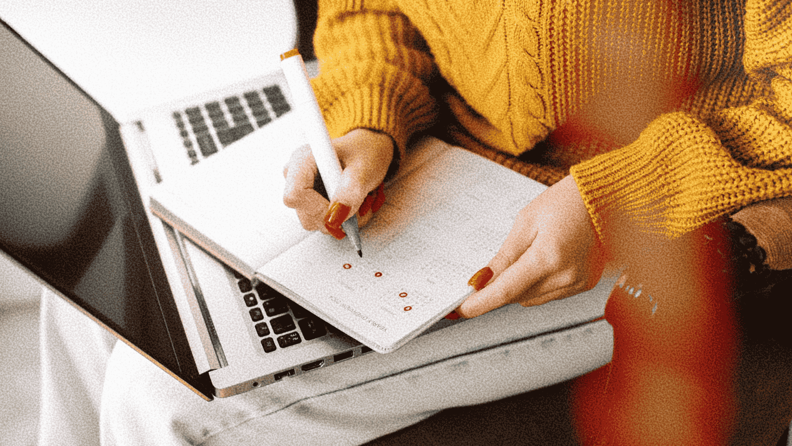woman seated with a laptop on her life, writing in a planner on top of the laptop