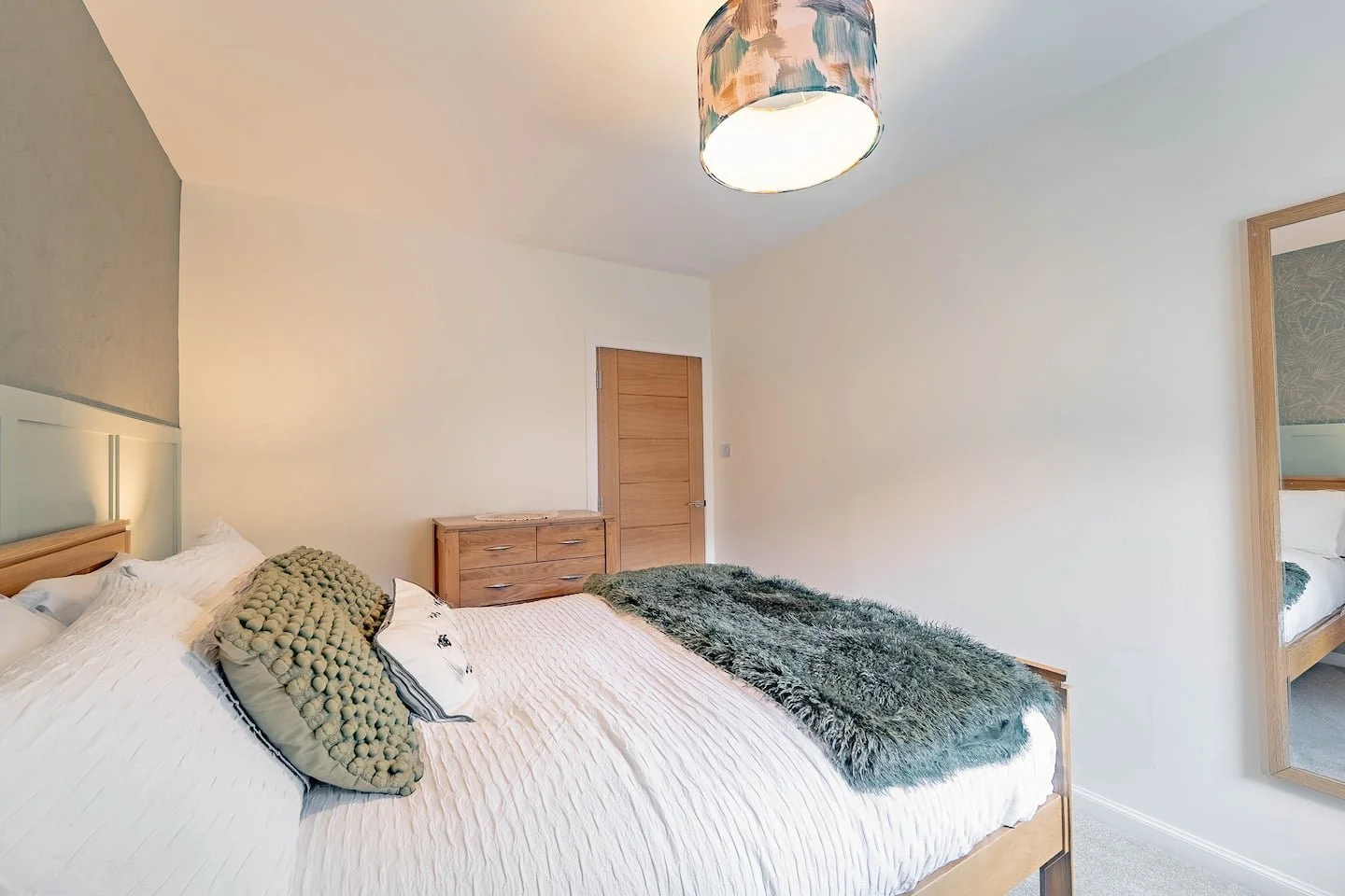 A bedroom with a large bed, wooden furniture, a decorative ceiling light, and a mirror on the wall.
