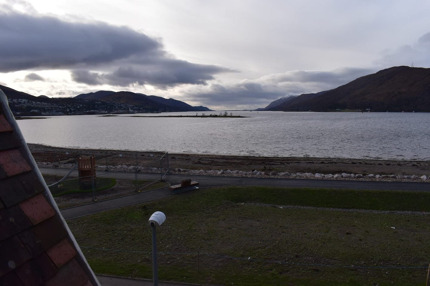 View of a large lake, mountains in the distance, cloudy sky, grassy area, and a small playground in the foreground.