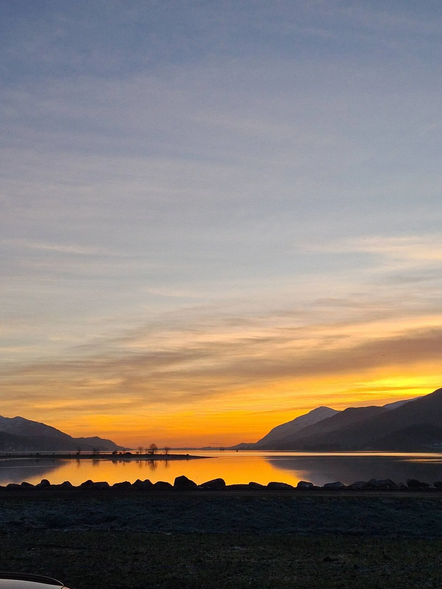 Sunset over a lake with mountains in the background and rocks along the shoreline.