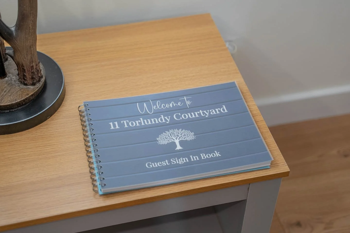 Guest sign-in book with the title 'Welcome to 11 Torlundy Courtyard' resting on a wooden table.