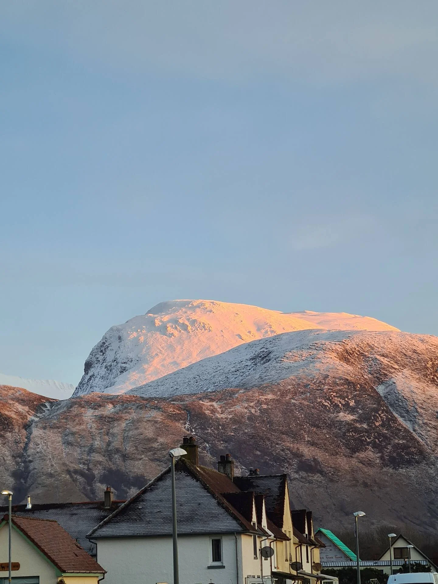 Snow-capped mountains in the background with a small town in the foreground including houses and streetlights.