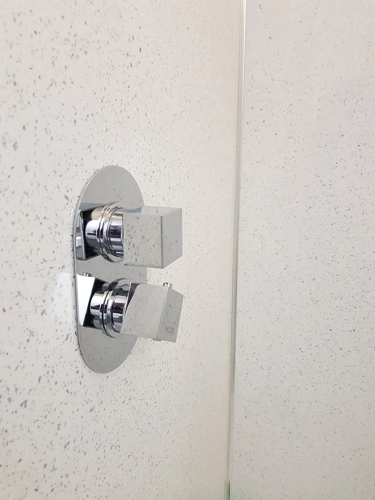 Close-up of a chrome shower control knob on a speckled white wall.