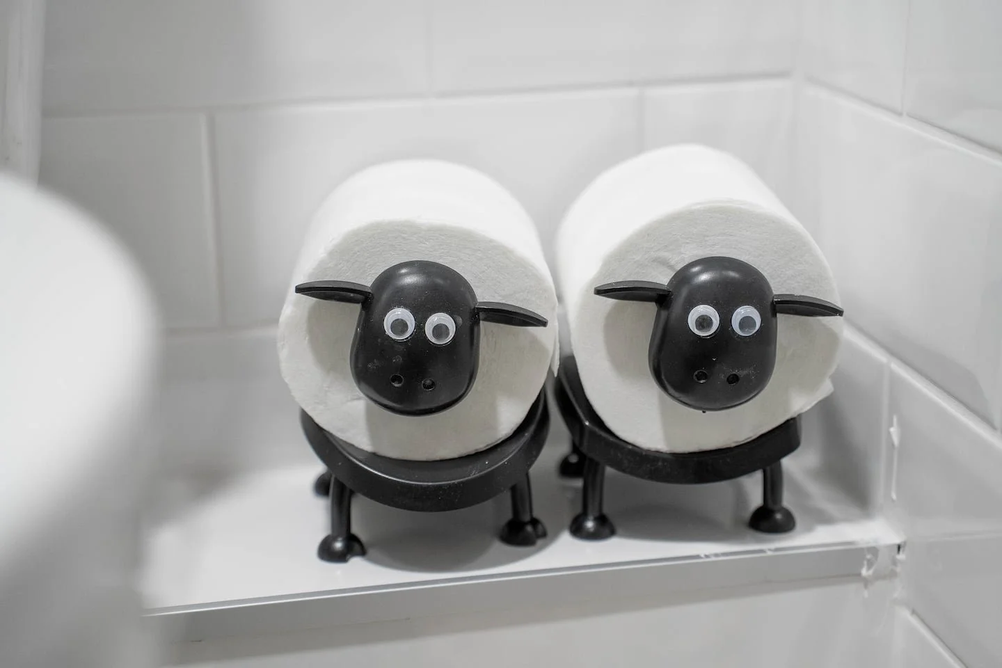 Decorative sheep made from toilet paper rolls with googly eyes and black plastic heads, placed on a bathroom shelf.