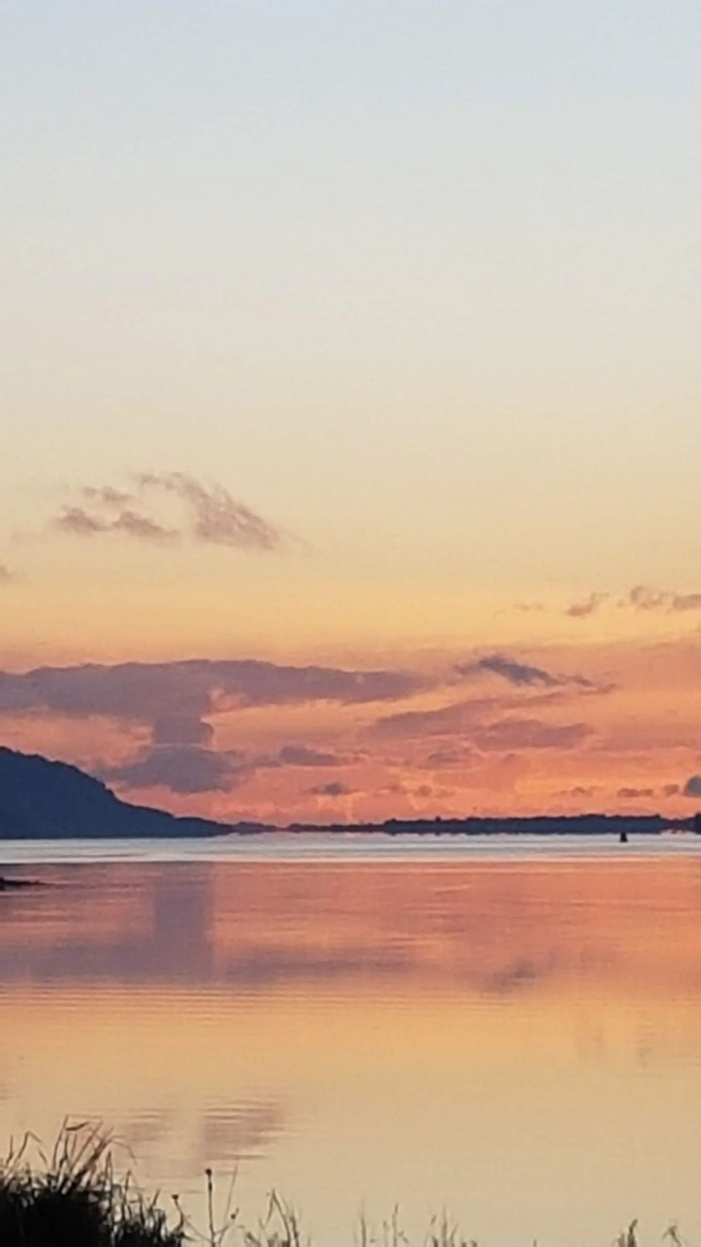 A peaceful sunset over a calm river, with reflections of the orange and pink sky and distant mountains.