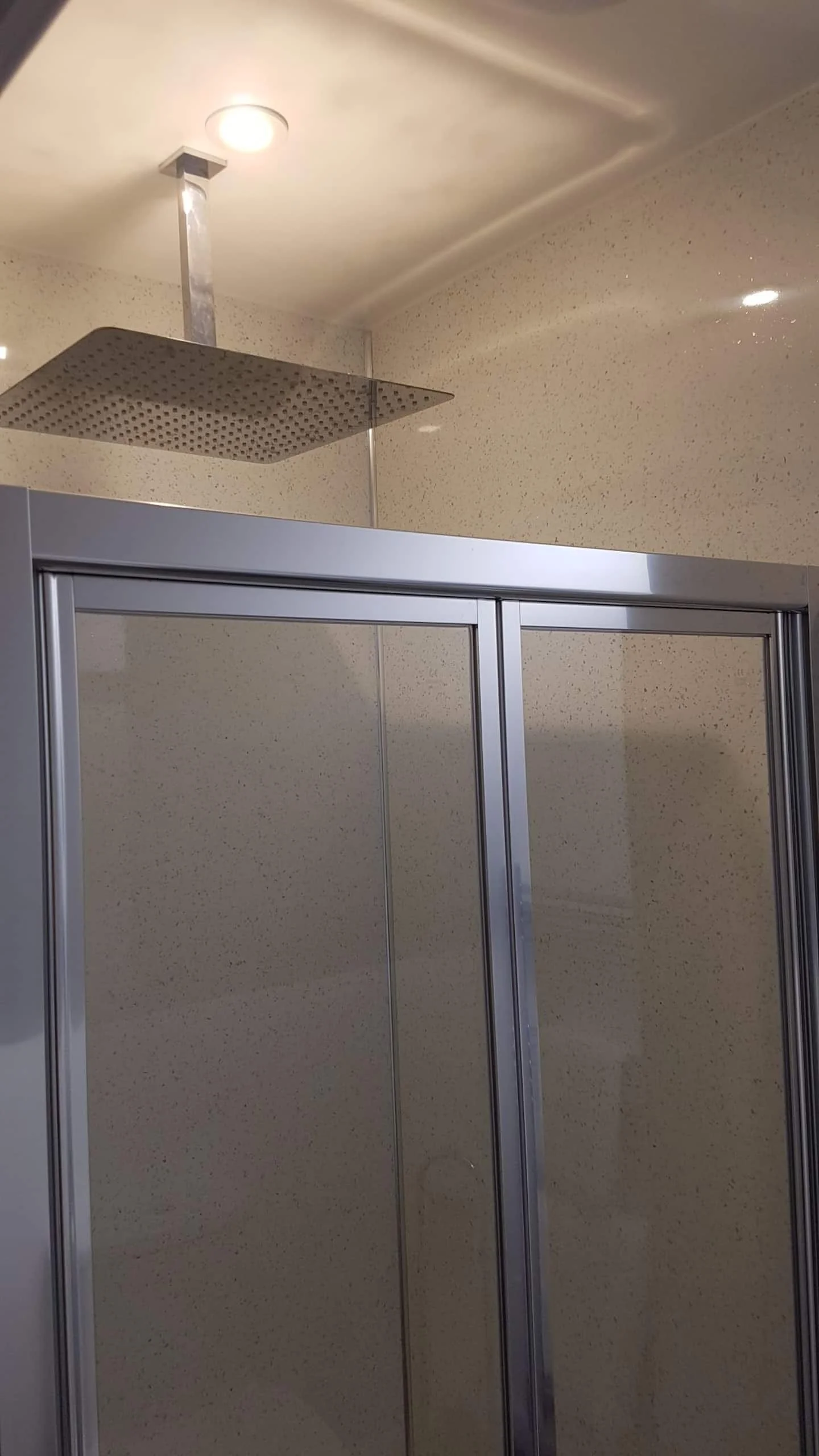 Shower with a square ceiling-mounted rainfall showerhead and a metal-framed sliding glass door.