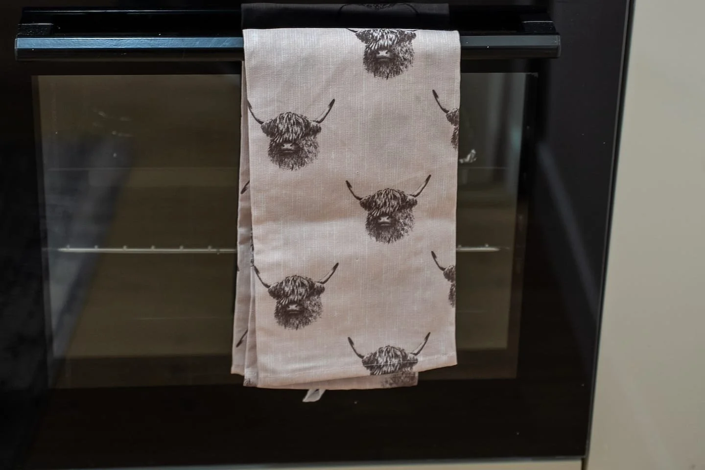 Oven with a beige kitchen towel featuring a black buffalo head pattern hanging on the handle.
