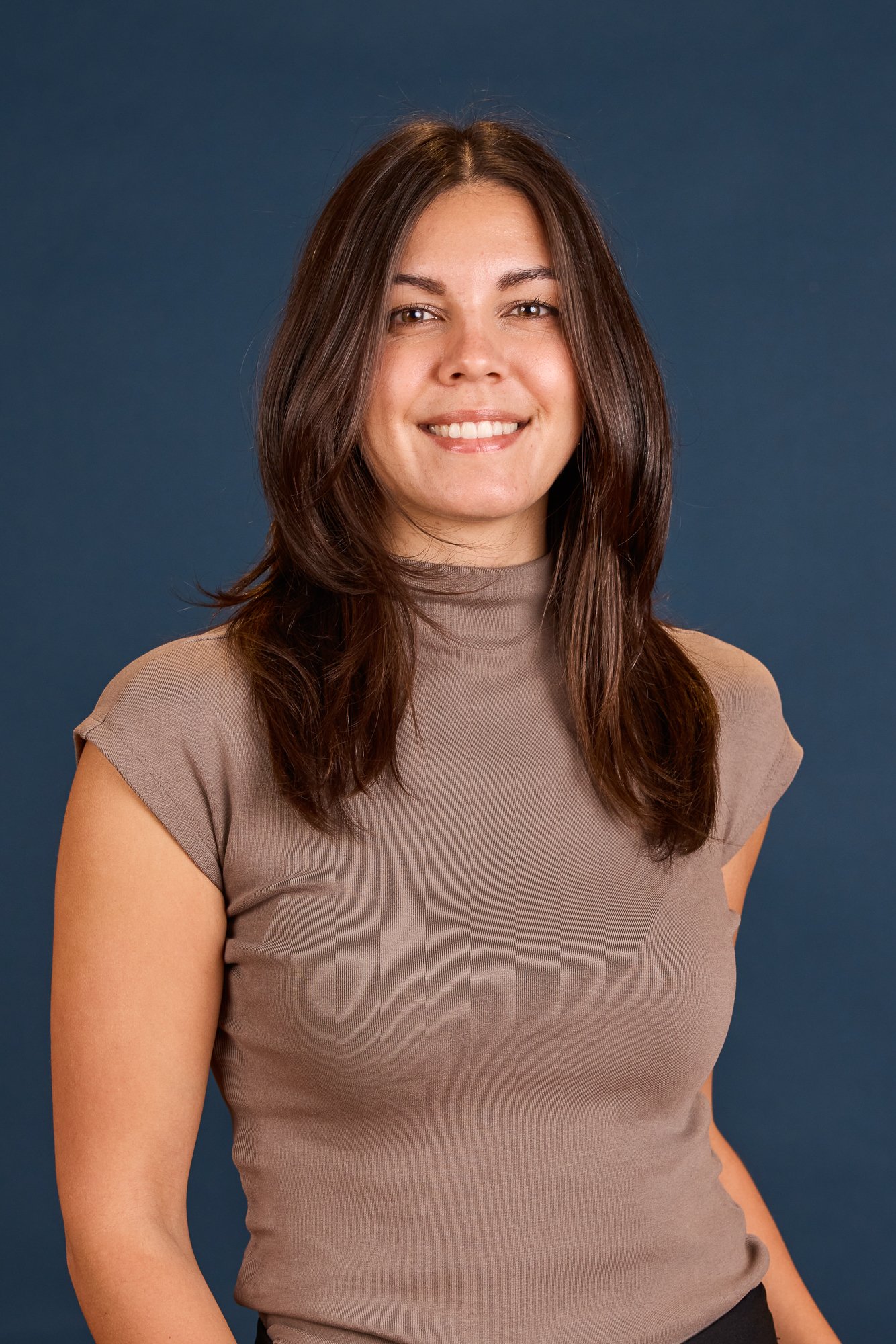 Fortgeschrittene Portraitaufnahme einer lachenden Frau mit braunen, mittellangen Haaren vor einem dunkelblauen Hintergrund.